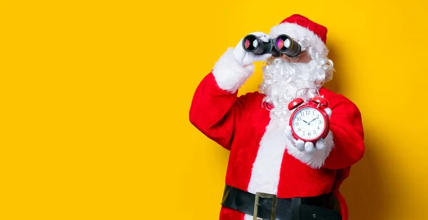 Santa Claus holding binoculars and alarm clock — Stock Photo, Image