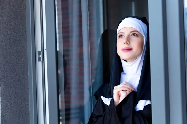 Jovem freira sorridente perto da janela — Fotografia de Stock
