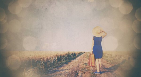 Brunette girl in blue dress with suitcase at countryside road