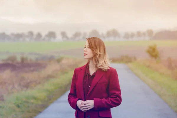 Roodharige vrouw in rode jas op platteland — Stockfoto
