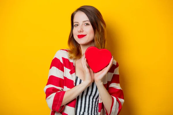 黄色の背景にバレンタインの日の若い赤毛の女性を示すハート型ギフト ボックス笑みを浮かべてください — ストック写真