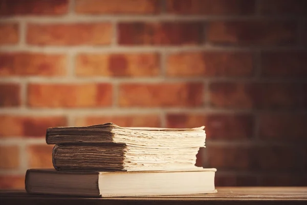 Vecchi libri su tavolo di legno a muro di mattoni — Foto Stock