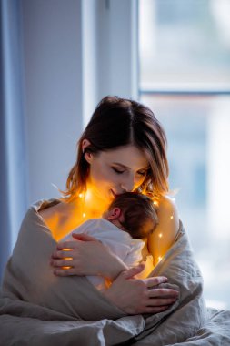 Anne ve bebek yatakta battaniyeye sarılmış. Ev iç
