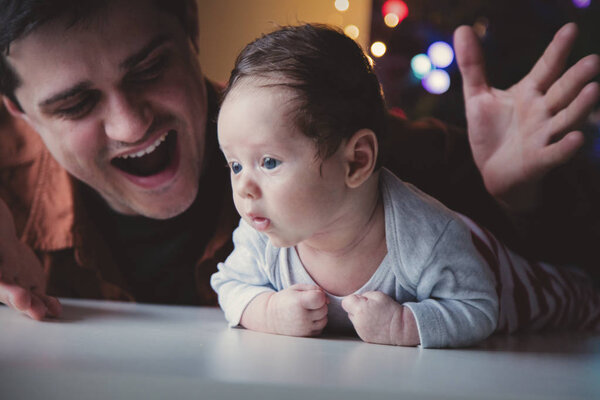 Young father help to a little child lie down on tummy in first time. Indoor image with focus on infant