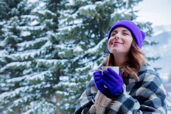 portrait of redhead girl in plaid and purple hat with cup of hot drink at winter outdoor