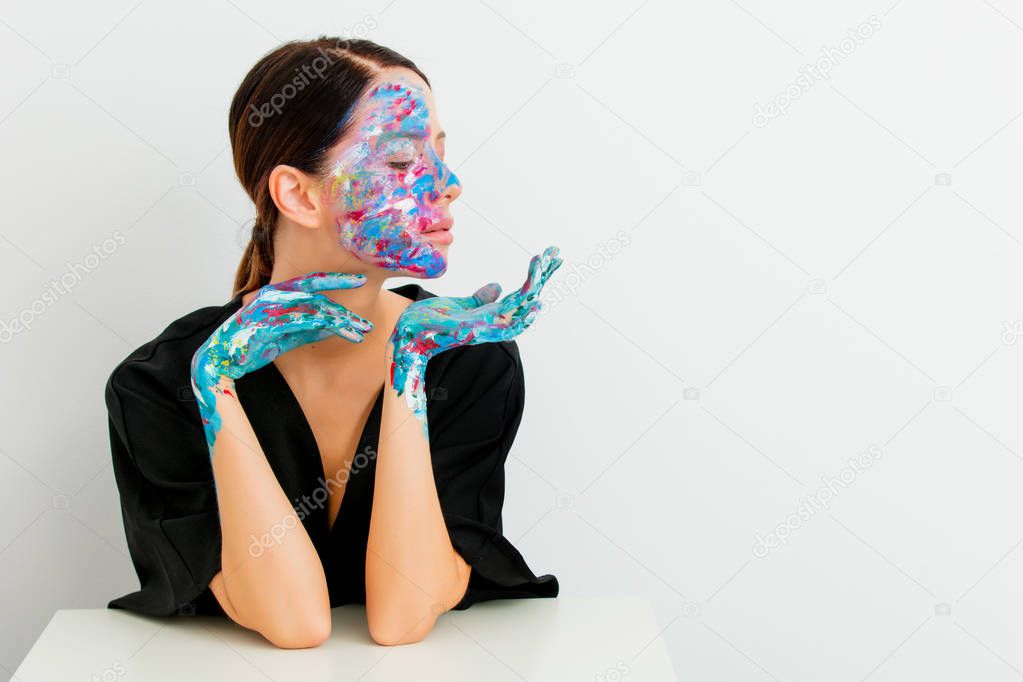 Pretty redhead caucasian woman in black dress and painted hands and face sitting at white table in lagom style on white background