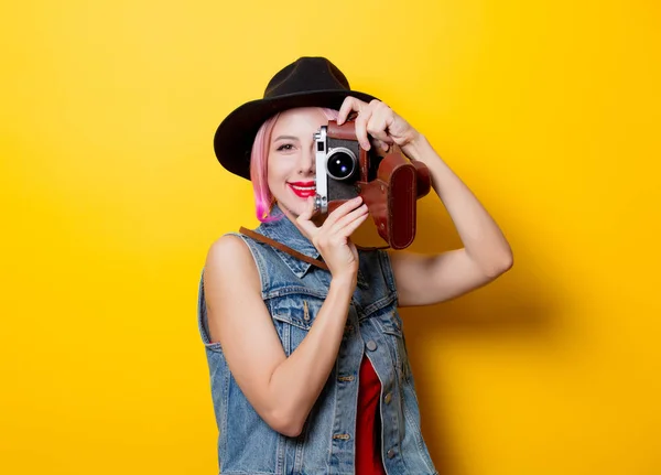 黄色の背景にレトロなカメラでピンクの髪型と若いスタイル内気な少女の肖像画 — ストック写真