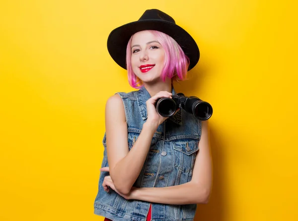 黄色の背景に双眼鏡でピンク髪スタイルを持つ若いスタイル流行に敏感な女の子の肖像画 — ストック写真