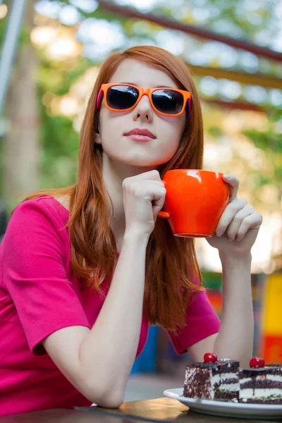 美丽的红头发女孩与蛋糕和范围杯子在咖啡馆在春天时间 — 图库照片