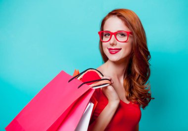 Genç beautfiul Kızıl saçlı kız gözlük ile mavi arka plan üzerinde alışveriş torbaları