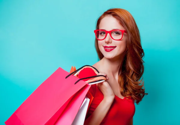 年轻的 Beautfiul 红头发的女孩在眼镜与购物袋在蓝色背景 — 图库照片