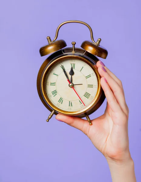 紫の背景にビンテージの目覚まし時計を持っている女性の手 — ストック写真