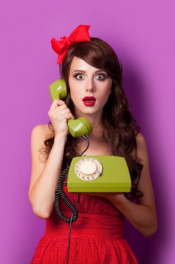 Kırmızı elbise ve yay ile yeşil sabit telefonu cep telefonu mor arka planda tutan genç brunet kız 