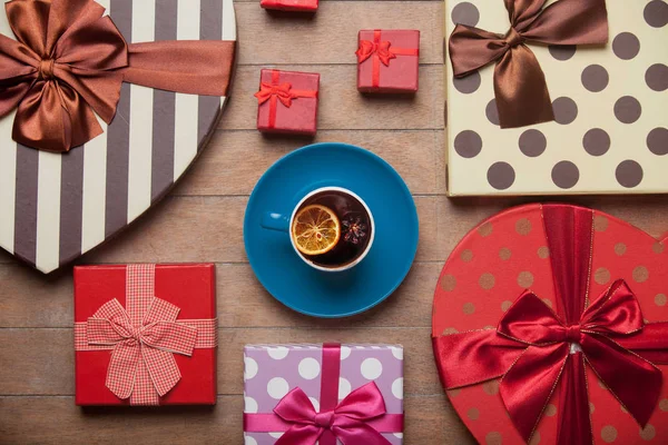 Cup of tea with lemon and holiday boxes on wooden background
