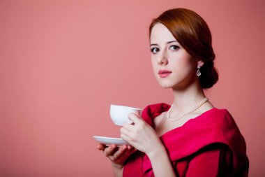 Çay pembe bir arka plan üzerinde kırmızı Viktorya dönemi kıyafetlerine genç Kızıl saçlı kadın