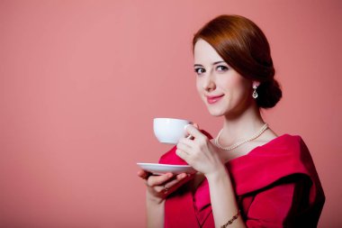 Çay pembe bir arka plan üzerinde kırmızı Viktorya dönemi kıyafetlerine genç Kızıl saçlı kadın