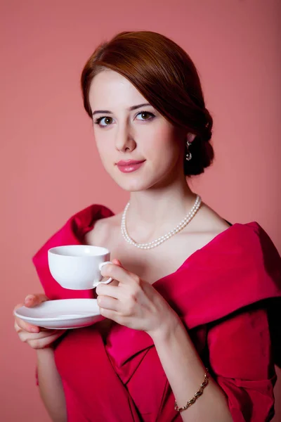 红色维多利亚时代的年轻红头发的妇女与杯茶在粉红色背景 — 图库照片