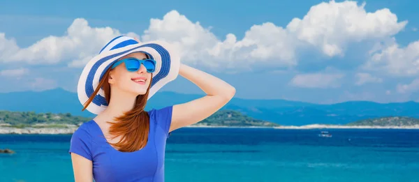 帽子と青い空と海の背景にサングラスで赤毛の女の子の肖像画 — ストック写真