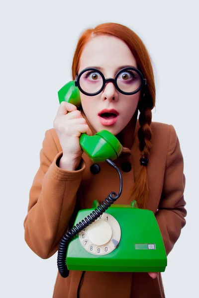 眼鏡と白い背景で電話で話してコートを持つ若い赤毛面白いオタク少女の肖像画 — ストック写真