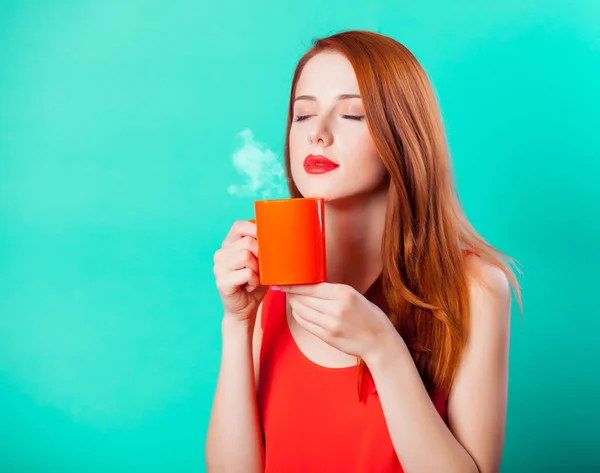 アクアマリン色の背景でコーヒーまたは紅茶のサンゴのカップで赤毛の女の子 — ストック写真