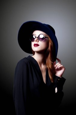 Güneş gözlüğü ve şapka gri arka plan üzerinde karanlık tarzı genç Kızıl saçlı kız 
