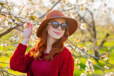 Şapka ve güneş gözlüğü çiçeği kiraz bahçesinde Kızıl saçlı kız. Bahar görüntü