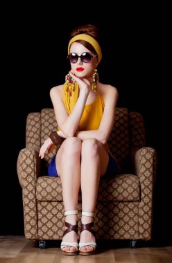 70 li yıllarda genç Kızıl saçlı kız siyah arka plan üzerine sandalyede oturan tarzı giysiler 