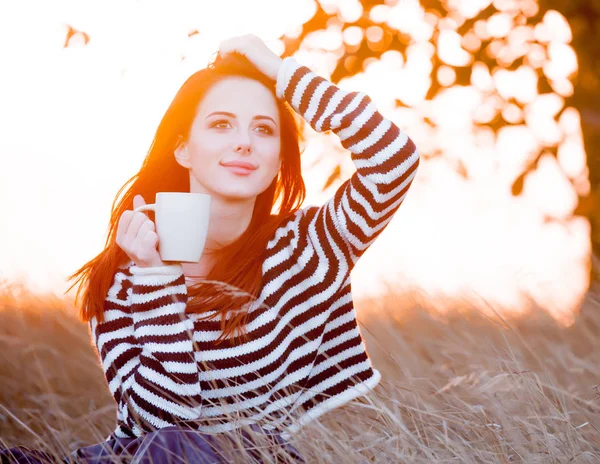 秋の公園で芝生の上に座ってコーヒーのカップを保持している若い女性 — ストック写真