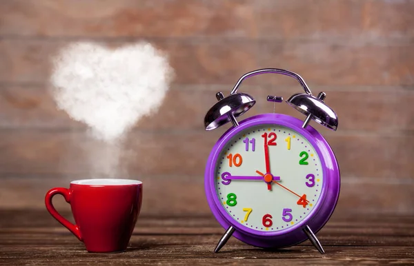 ハート形蒸気と木製のテーブルの上の目覚まし時計とコーヒーの赤カップ — ストック写真