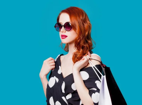 青の背景にショッピング バッグにサングラスの赤毛の女性 — ストック写真