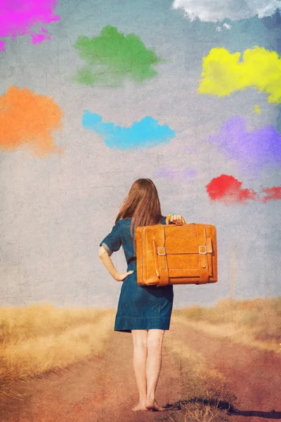 カラフルな雲と夏の間は田舎で道を歩いてスーツケースとブルネットの少女 — ストック写真