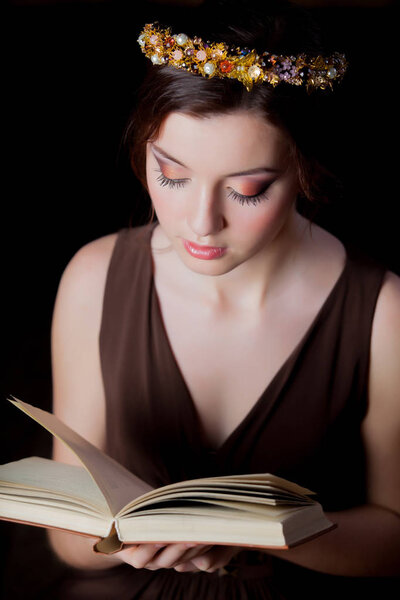 Young brunette woman with wreath and book on black background.