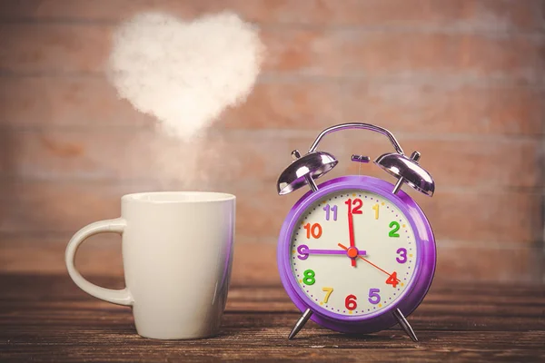 ハート形蒸気と木製のテーブルの上の目覚まし時計とコーヒーの白いカップ — ストック写真