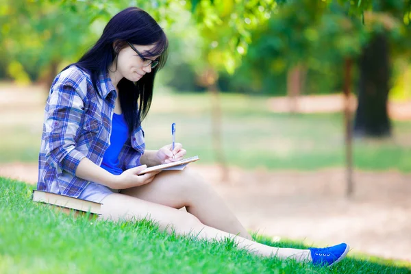 夏の間は緑の草の勉強ノートでブルネットの学生の若い女の子 — ストック写真