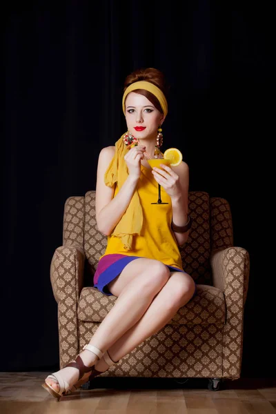 年代の若い赤毛の女の子黄色黒の背景でカクテルと肘掛け椅子に座って服スタイル — ストック写真
