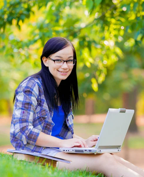 ラップトップ コンピューターの夏の緑の草の上勉強とブルネットの学生の若い女の子 — ストック写真