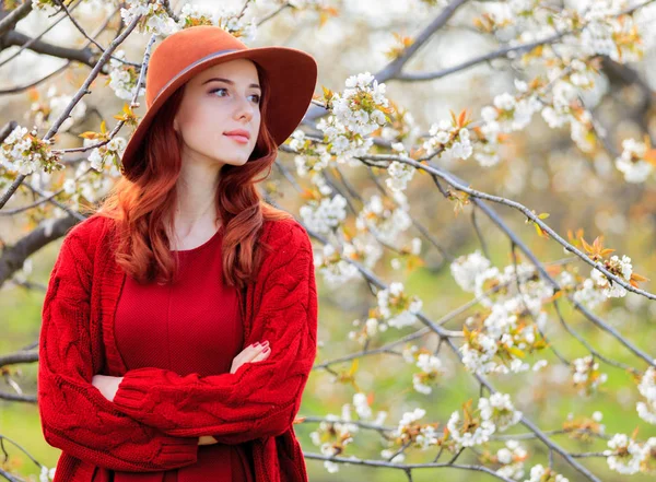 红色衣裳和帽子站立在绽放的庭院的年轻妇女 — 图库照片