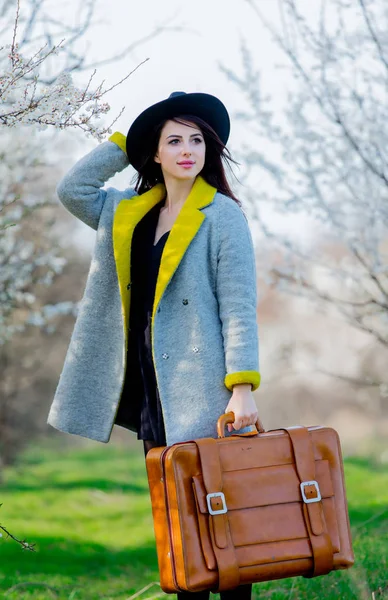 コートと屋外春のスーツケースと帽子で若い赤毛の女の子 — ストック写真
