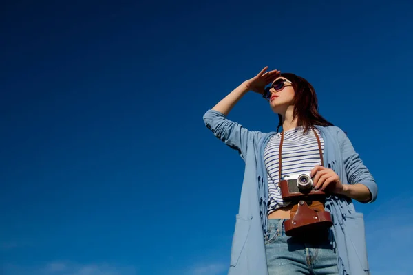 年轻风格的红发女孩在现代服装与相机在蓝天与云背景 — 图库照片