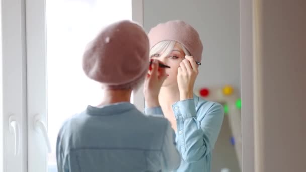 年轻的女孩在短头发贝雷帽在家里的镜子附近应用化妆 — 图库视频影像