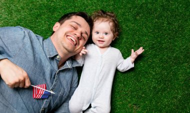 Baba ve oğul ABD bayrağı ile yeşil çimenlerin üzerinde uzanmış.