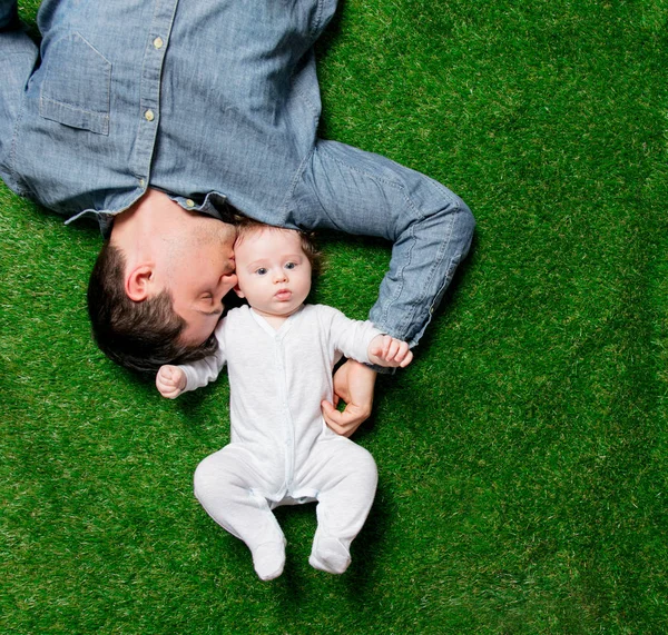若い父親と息子が緑の芝生に横になって — ストック写真