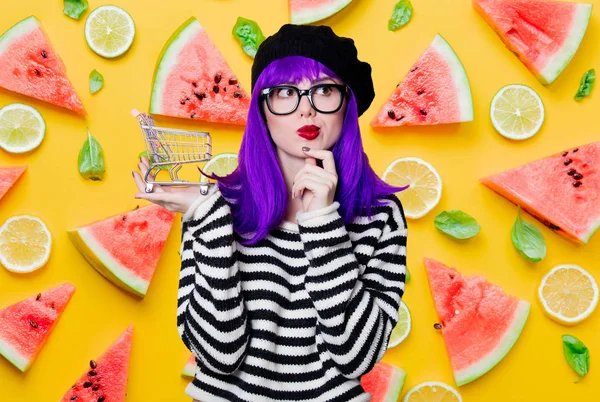 紫の髪と黄色の背景のショッピングカートを持つ若い女性の肖像画 — ストック写真