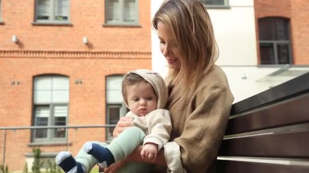 Молода мама і дитина сидять на лавці — стокове відео