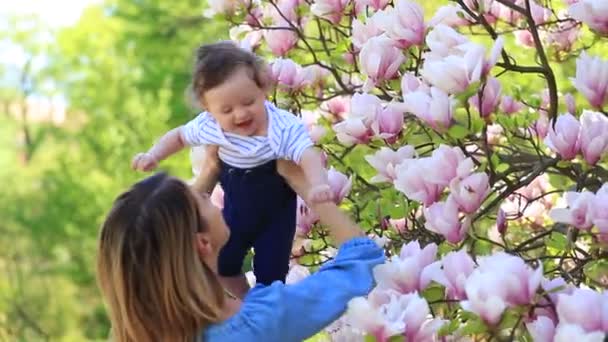年轻的红头发的母亲和孩子在阳光明媚的日子里有一个悠闲的春天木兰开花花园 — 图库视频影像