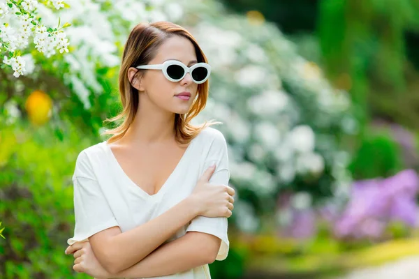 Rödhårig tjej i vita solglasögon nära blommor — Stockfoto