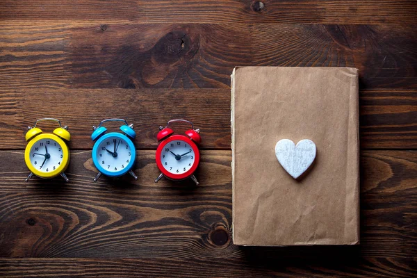 Três relógios de alarme coloridos e livro com forma de coração — Fotografia de Stock