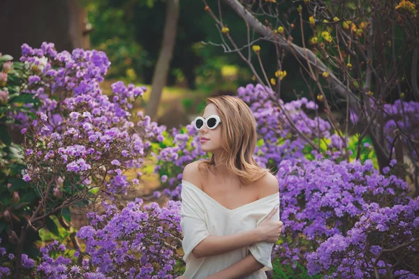 Menina em óculos de sol brancos perto de flores roxas — Fotografia de Stock