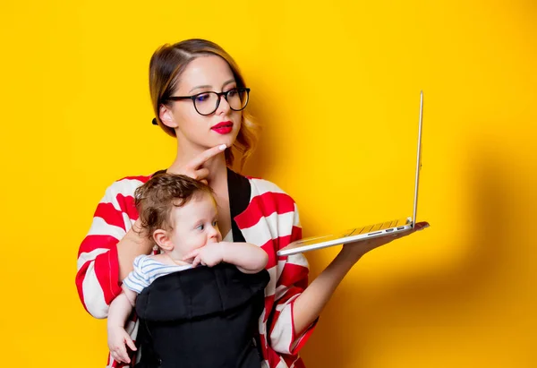 Pequeno bebê em portador e mãe com laptop — Fotografia de Stock