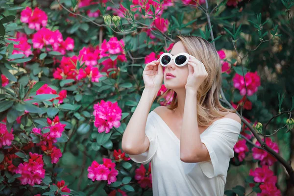 Roodharige meisje in witte zonnebril in de buurt van bloemen — Stockfoto